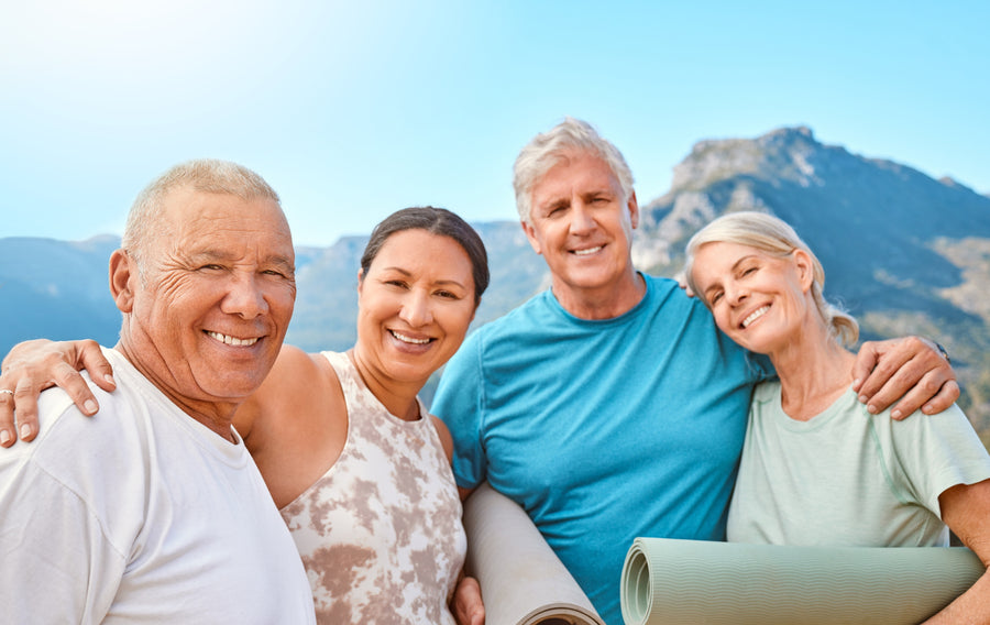 Group of smiling senior friends at a yoga retreat, enjoying each other's company before or after an outdoor group yoga session in a natural setting