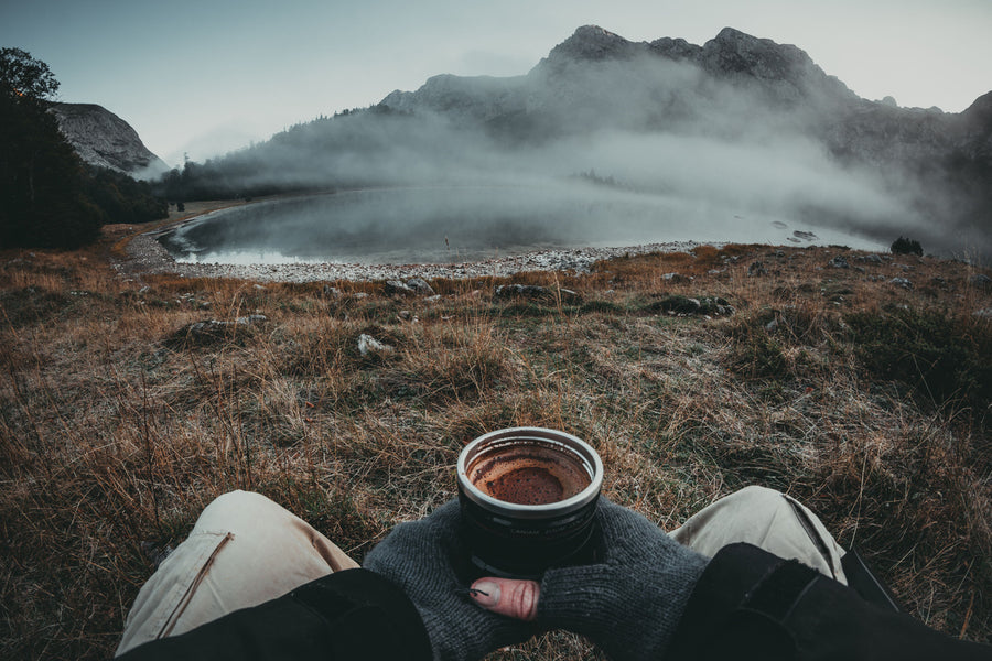 POV shot of an individual appreciating a breathtaking mountain landscape while holding a steaming cup of coffee